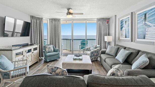 A spacious living room with a large flat-screen TV, comfortable seating, a ceiling fan, and a view of the ocean through large sliding doors. - Stunning condo with updates galore, oceanfront view | AshWorth - 1805 (North Myrtle Beach)