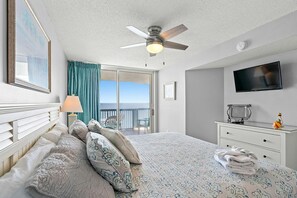 A bedroom with a bed, a ceiling fan, a TV, a dresser, and a view of the balcony. - Stunning condo with updates galore, oceanfront view | AshWorth - 1805 (North Myrtle Beach)