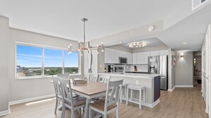 A modern kitchen with white cabinetry, a central island, and a dining area with a wooden table and white chairs.
