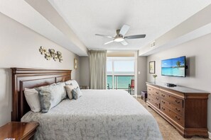 Ein Schlafzimmer mit Bett, Schminktisch, Deckenventilator, Fernseher und Meerblick.