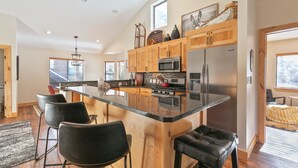 A modern kitchen with a large island, wooden cabinets, stainless steel appliances, and a view to the outside.