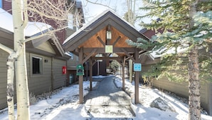 A covered outdoor area with a wooden structure, a pathway leading to a building, and a sign indicating parking availability.