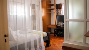 A bedroom with a bed, a wooden wardrobe, a small table, and a window with curtains. - Celio Jardine Lavington (Nairobi)