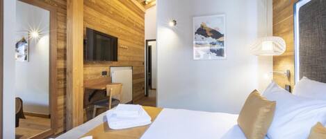 A hotel room with a wooden ceiling, a bed with white linens, a desk with a chair, and a television.