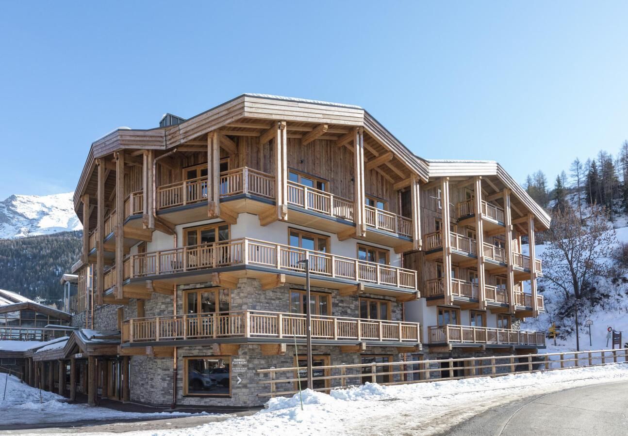 A multi-story wooden building with balconies, likely a hotel or lodge, surrounded by snow and mountains.