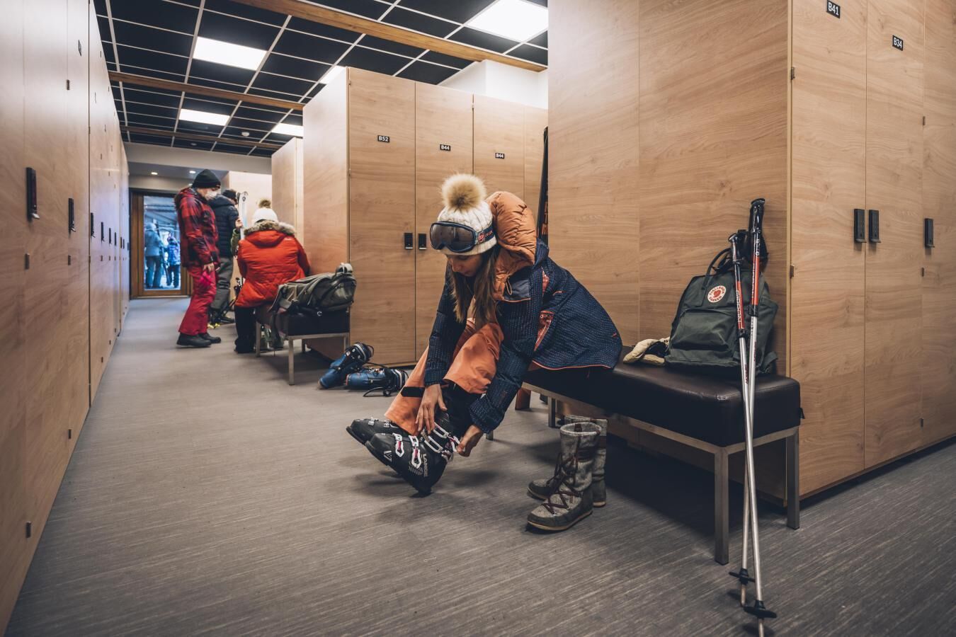 A hallway with lockers, benches, and a person adjusting shoes.