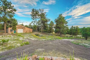 A single-story building with a garage, surrounded by a fenced area with trees and a gravel driveway. - Nature's Oasis, 4BD Ranch Retreat, Hot tub! (Peyton)