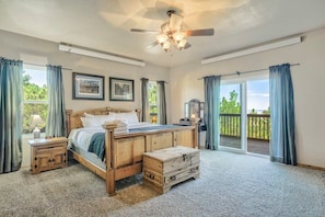 A bedroom with a wooden bed, a ceiling fan, a nightstand, a chest of drawers, and a view of the outdoors through a sliding glass door.