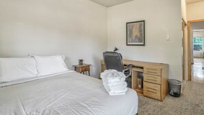 Ein Schlafzimmer mit einem Bett, einem Schreibtisch, einem Sessel und einem gerahmten Bild an der Wand.