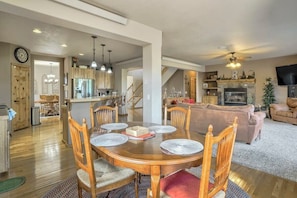 A spacious living area with a dining table set for four, a fireplace, and a television mounted on the wall.