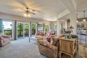 A spacious living room with a large sofa, a coffee table, and a wooden side table. There is a sliding glass door leading to a balcony with a view of greenery. - Nature's Oasis, 4BD Ranch Retreat, Hot tub! (Peyton)