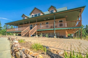 A two-story house with a covered porch and a stone retaining wall. - Nature's Oasis, 4BD Ranch Retreat, Hot tub! (Peyton)