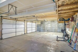 A garage with two large white garage doors, a concrete floor, and a wooden ceiling.