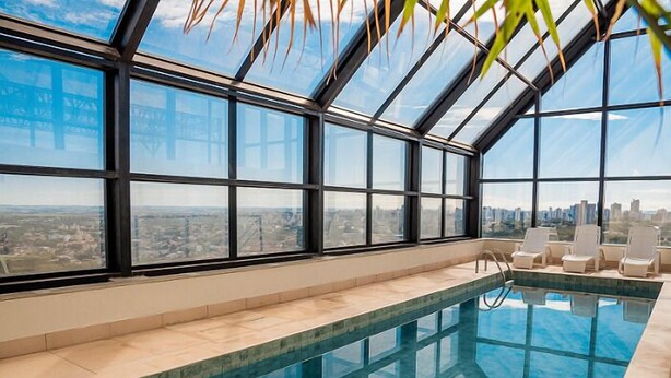 Une piscine intérieure avec vue sur la ville, de grandes fenêtres et des chaises longues.