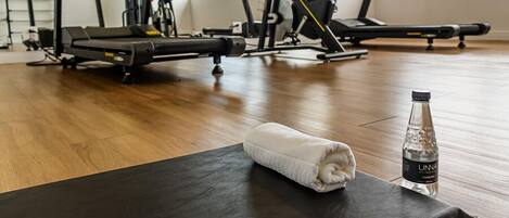 Une salle de sport avec des appareils d’exercice, une bouteille d’eau et une serviette sur un tapis.