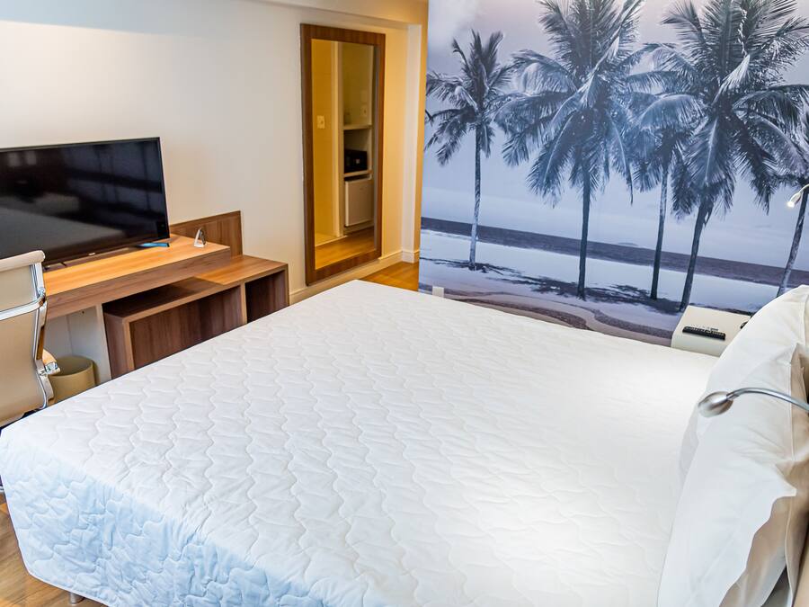 A hotel room with a bed, a desk with a TV, and a door leading to a bathroom.