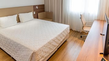 Una habitación de hotel con una cama grande, un escritorio de madera, una silla y un televisor.