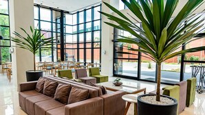 Un hall d’entrée spacieux, avec un canapé marron, des fauteuils verts et une grande plante en pot.