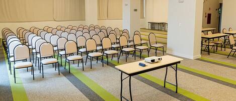A conference room with rows of chairs and tables, carpeted floor, and a large window.