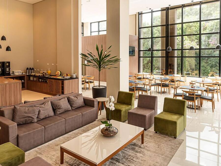 Un moderno vestíbulo de hotel con un área de descanso, un bar y grandes ventanales con vistas al exterior.