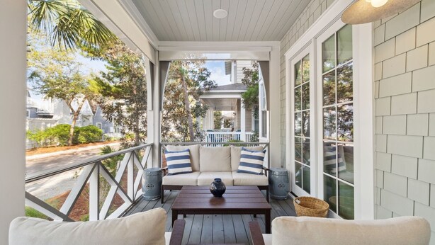 A covered outdoor seating area with a sofa and chairs, a table, and a view of a residential street. - Beach Access and Private Pool (Watersound)