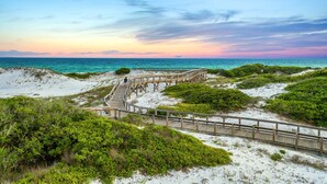 A wooden boardwalk leading to a beach with white sand and green vegetation. - Beach Access and Private Pool (Watersound)