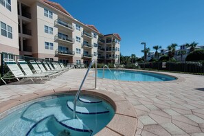 A pool area with lounge chairs and a building with balconies in the background.
