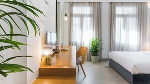 Une chambre d’hôtel moderne avec un bureau en bois, une chaise, un lit et une grande fenêtre avec des rideaux.