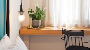 Une pièce avec une fenêtre, une plante posée sur un rebord en bois, une chaise noire et un lit avec une literie blanche.