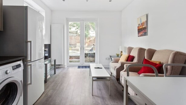 A modern kitchen with a washing machine, a dining area with a table and chairs, and a sofa with cushions. - Modern 2 bed in Wembley - 30 min to central London (Greater London)