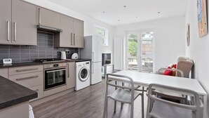 A modern kitchen with grey cabinets, a built-in oven, a washing machine, and a dining area with a white table and chairs. - Modern 2 bed in Wembley - 30 min to central London (Greater London)