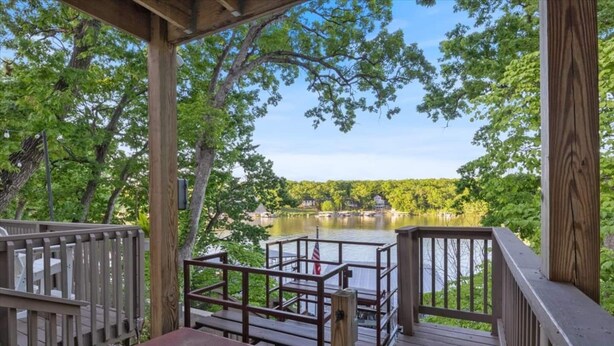 A wooden deck with a view of a lake and a house in the background. - The Anchor House — Experience lakeside luxury at a spacious 5-bedroom retreat in Osage Beach. Enjoy breathtaking views, modern comforts, and direct lake access for the perfect Lake of the Ozarks getaway. (Osage Beach)