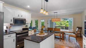 A modern kitchen with white cabinets, a central island, and a dining area with wooden chairs and a table. - The Anchor House — Experience lakeside luxury at a spacious 5-bedroom retreat in Osage Beach. Enjoy breathtaking views, modern comforts, and direct lake access for the perfect Lake of the Ozarks getaway. (Osage Beach)