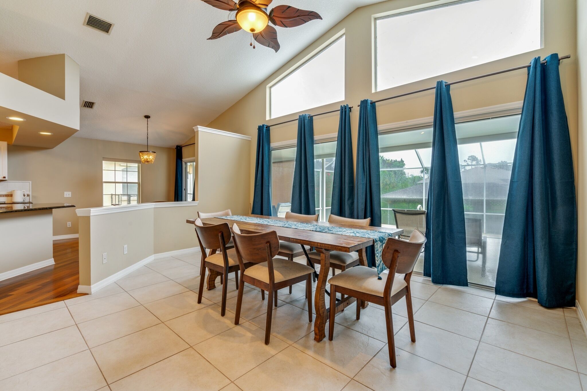 A dining area with a table and chairs, a ceiling fan, and large windows with curtains.