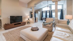 A spacious living area with a flat-screen TV, a wooden entertainment unit, a beige sofa, and a dining area with a table and chairs. - Peaceful Waterfront Pool Home 3 Bedroom Home by RedAwning (Palm Coast)
