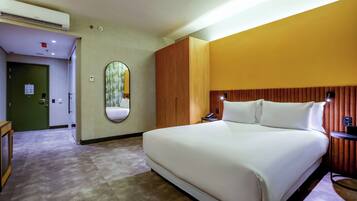 A hotel room with a large bed, a mirror, a wooden headboard, a bedside table, and a green door.