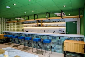 A bar area with a green ceiling, blue bar stools, and a marble countertop.