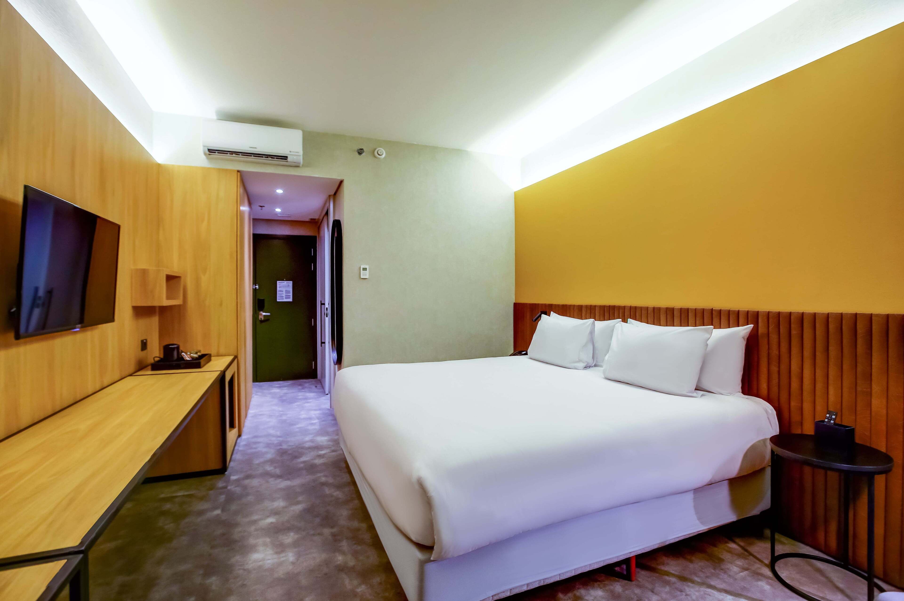 A hotel room with a bed, a desk, a television, and an air conditioning unit.