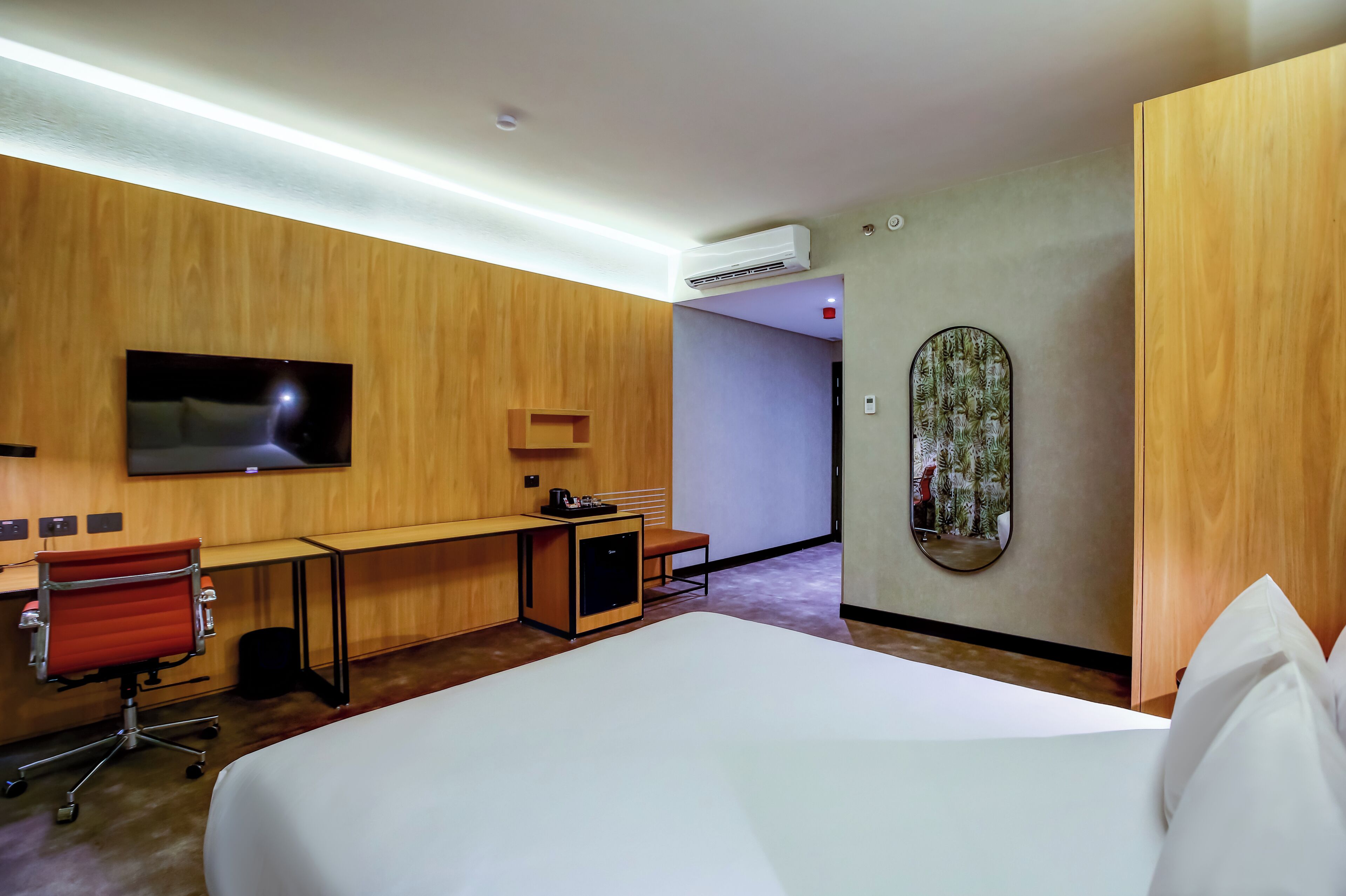 A hotel room with a bed, desk, chair, TV, and a small refrigerator.