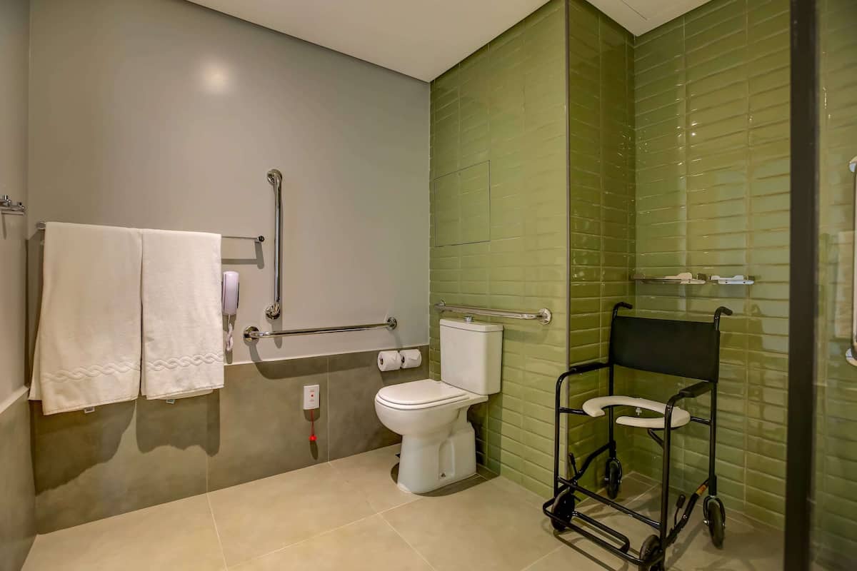 Une salle de bain équipée de toilettes, de barres d’appui, d’un fauteuil roulant et d’un porte-serviettes.