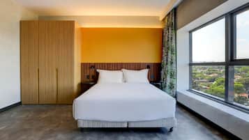 A modern hotel room with a large bed, a wooden wardrobe, and a city view through a large window.