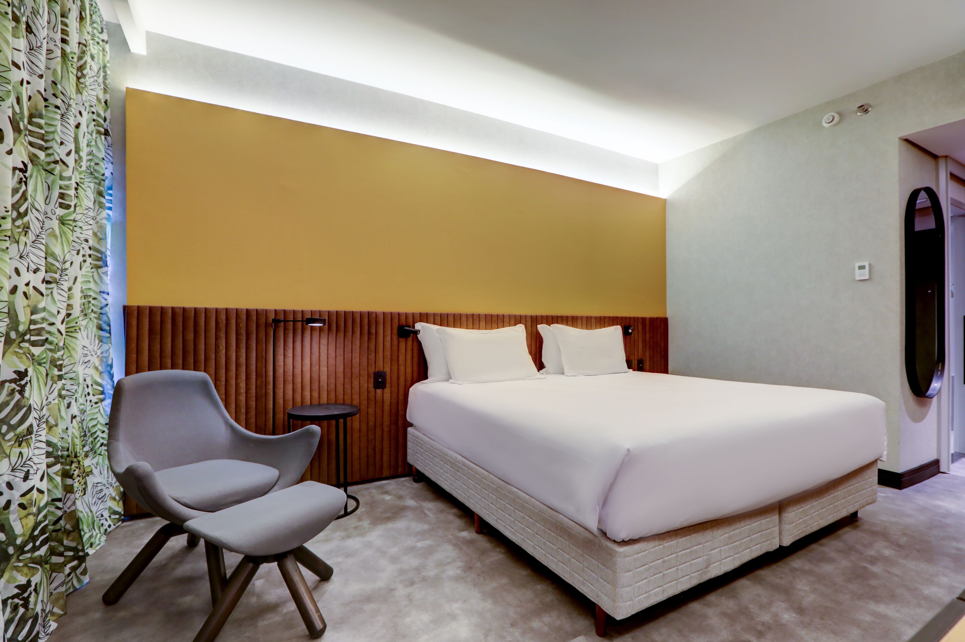 A hotel room with a large bed, a chair, a small table, and a curtain with a leaf pattern.