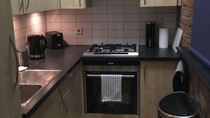 A compact kitchen with light wooden cabinets, a black countertop, a Siemens oven, a gas stove, a coffee maker, and a trash bin. - Stylish Open Plan Loft in Manchester City Centre (Manchester)