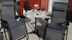 Ein Außenbereich mit Sitzgelegenheiten, zwei schwarzen Metallstühlen und einem Tisch, einem roten Zaun und einer weißen Tür.