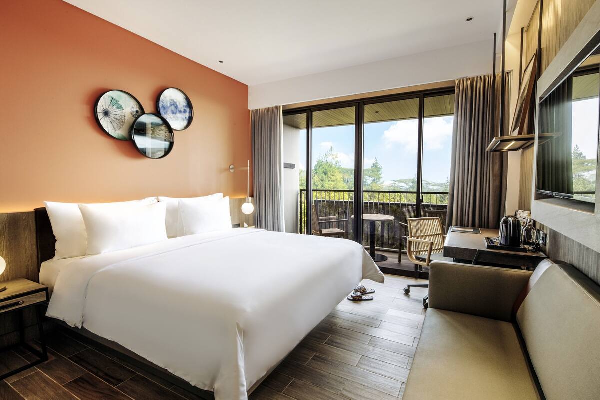 A hotel room with a large bed, a desk with a chair, and a balcony with a table and chairs.