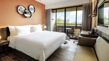 Una habitación de hotel con una cama grande, un escritorio con silla, y un balcón con mesa y sillas.