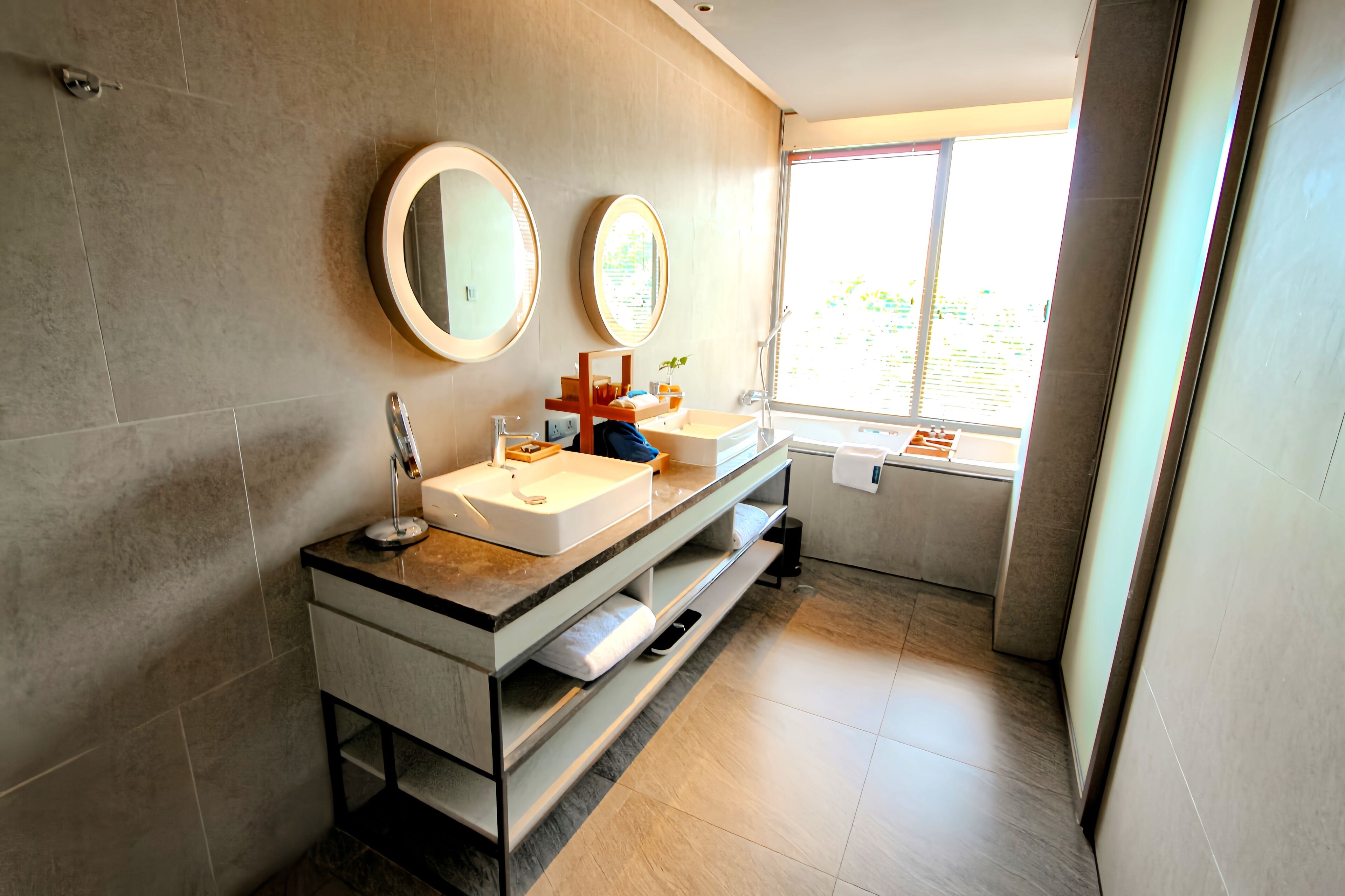 Un baño moderno con dos lavamanos, tocador y ventana que ofrece luz natural.