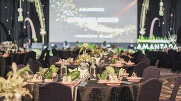A banquet hall with tables set for a formal event, decorated with plants and glassware.