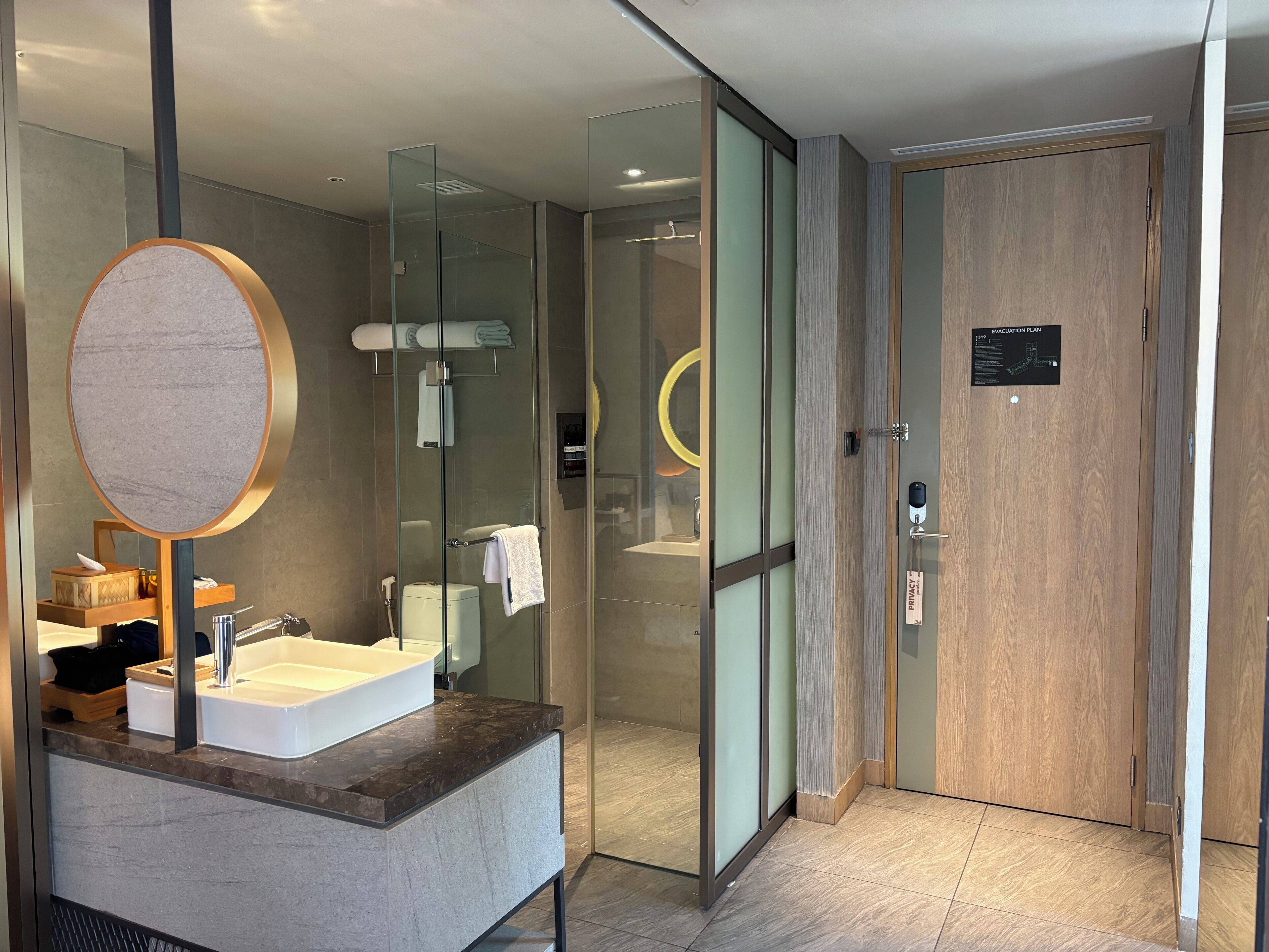A modern bathroom with a glass shower enclosure, a sink with a marble countertop, and a wooden door with a privacy label.
