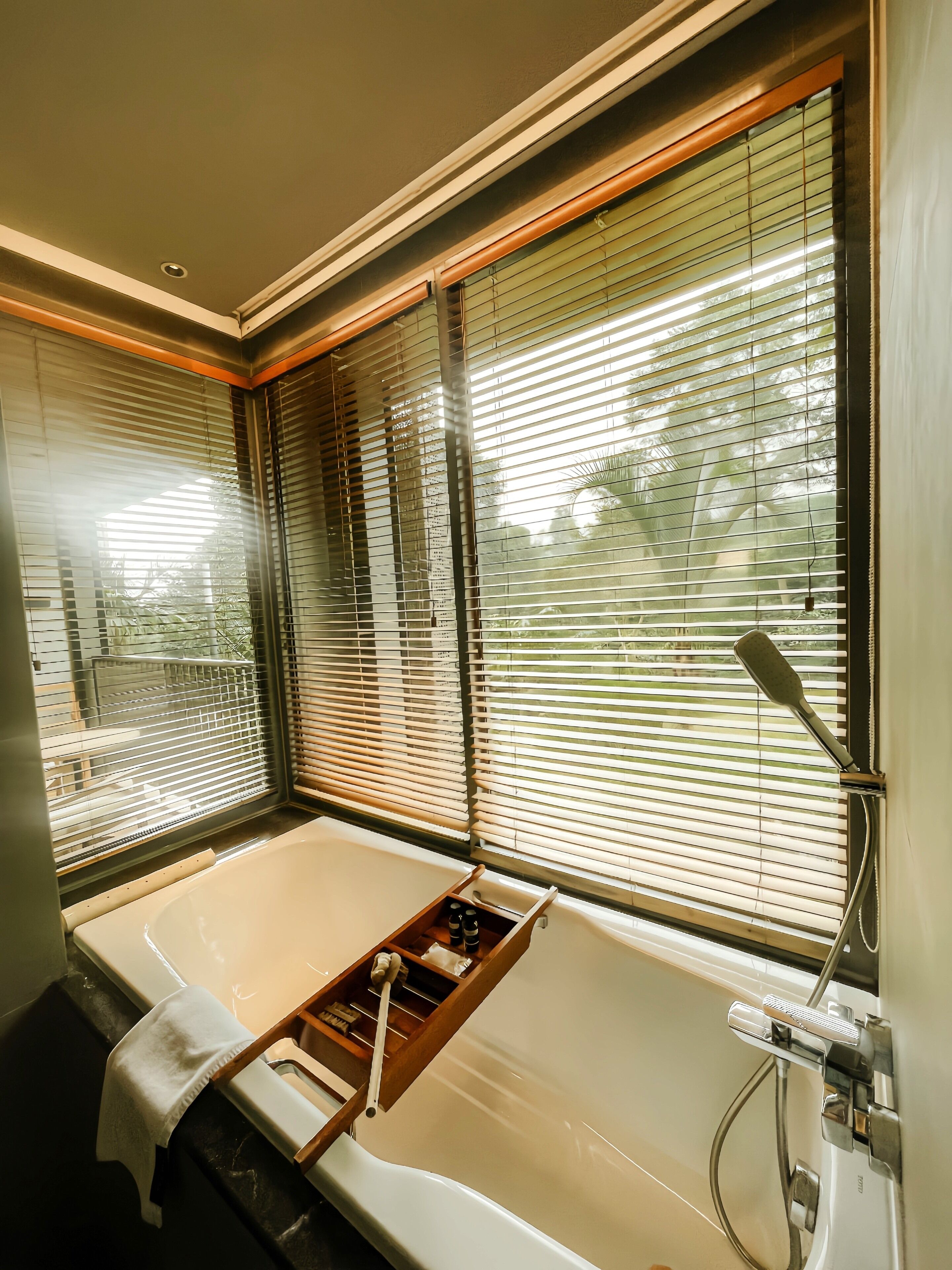 Une salle de bain avec une baignoire, des stores en bois aux fenêtres et un porte-serviettes.